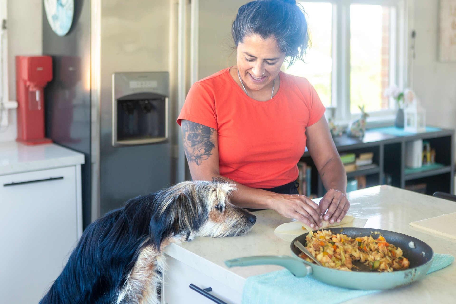 Woman preparing spring rolls with her dog watching in the kitchen